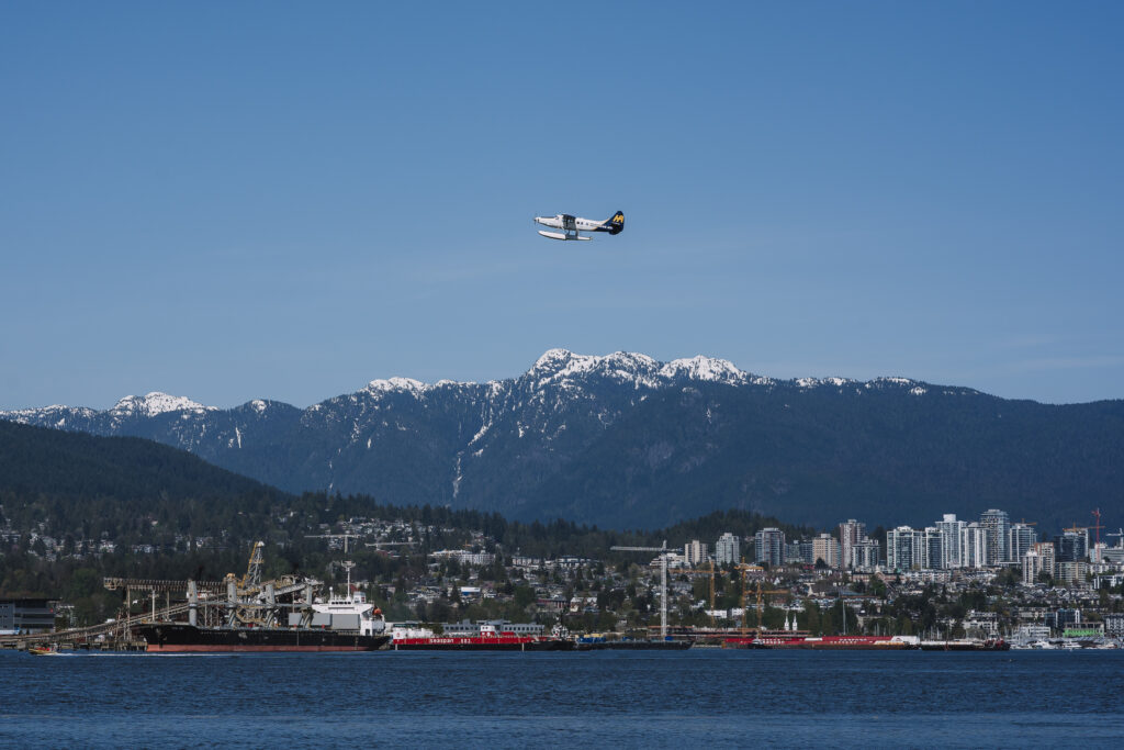 Panoramic view of North Shore Mountains and a seaplane flying over the waters near Stanley Park, Vancouver