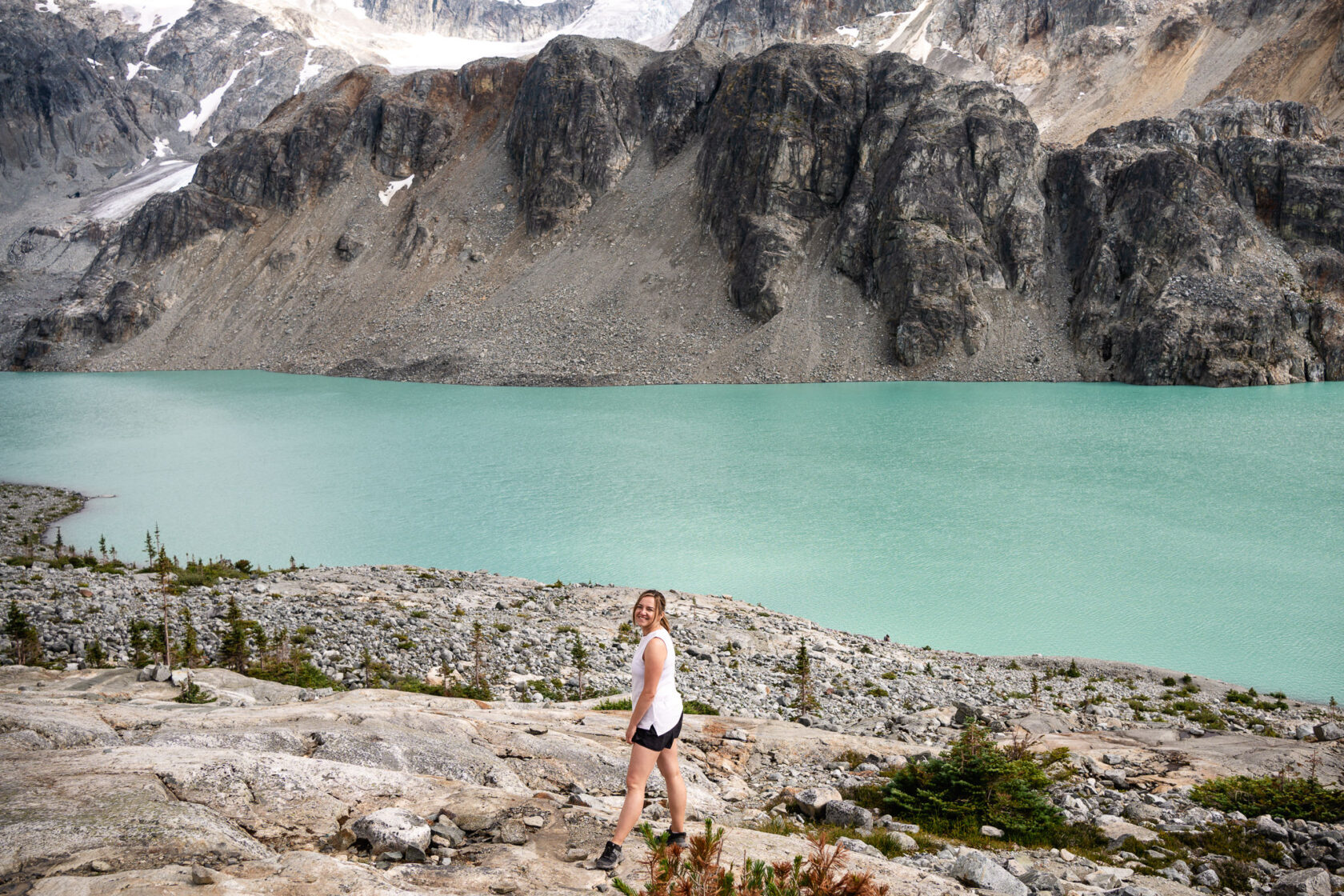 Happy hiker in the foreground, with a big smile, set against the stunning backdrop of the turquoise Wedgemount Lake