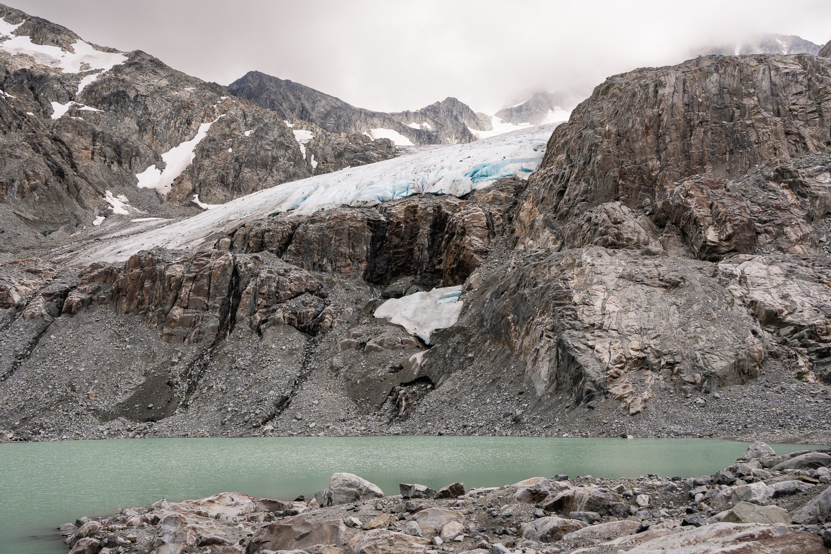 Tupper Lake beneath a cloudy sky, framed by the receded Wedgemount Glacier creating a serene and atmospheric scene