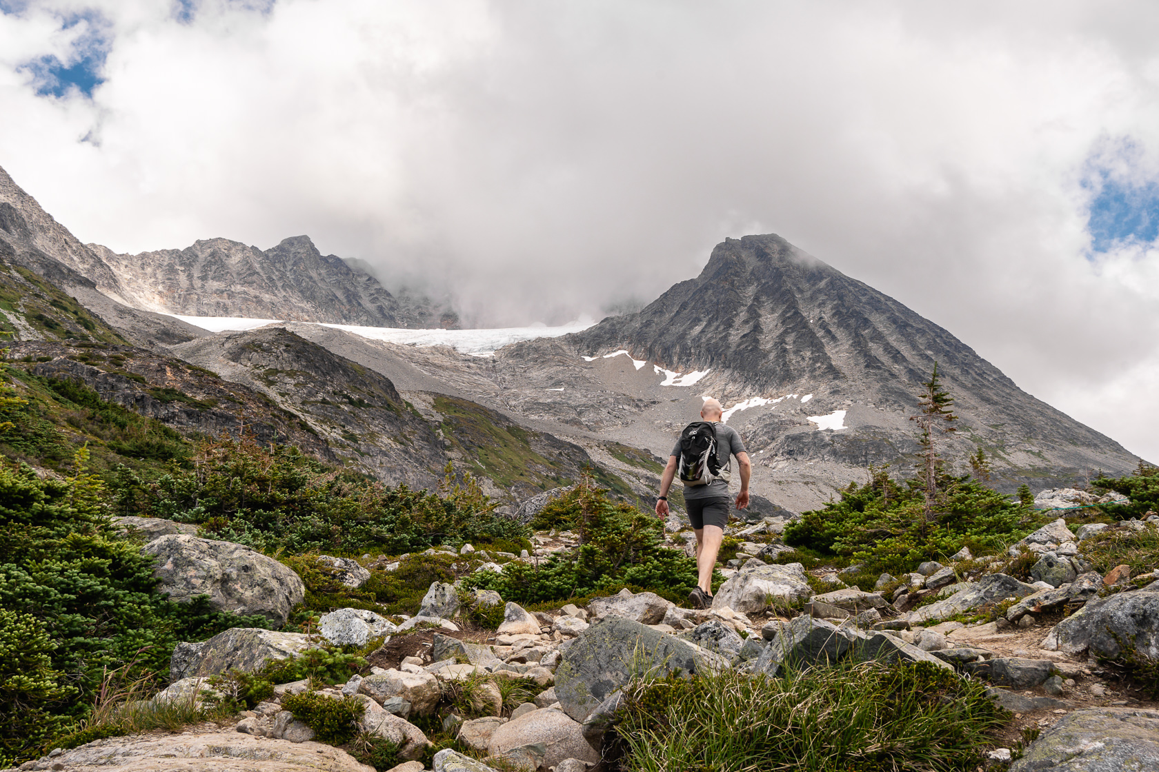 Hiker seen from behind, nearing the summit of Wedgemount Lake trail, surrounded by breathtaking mountain scenery 