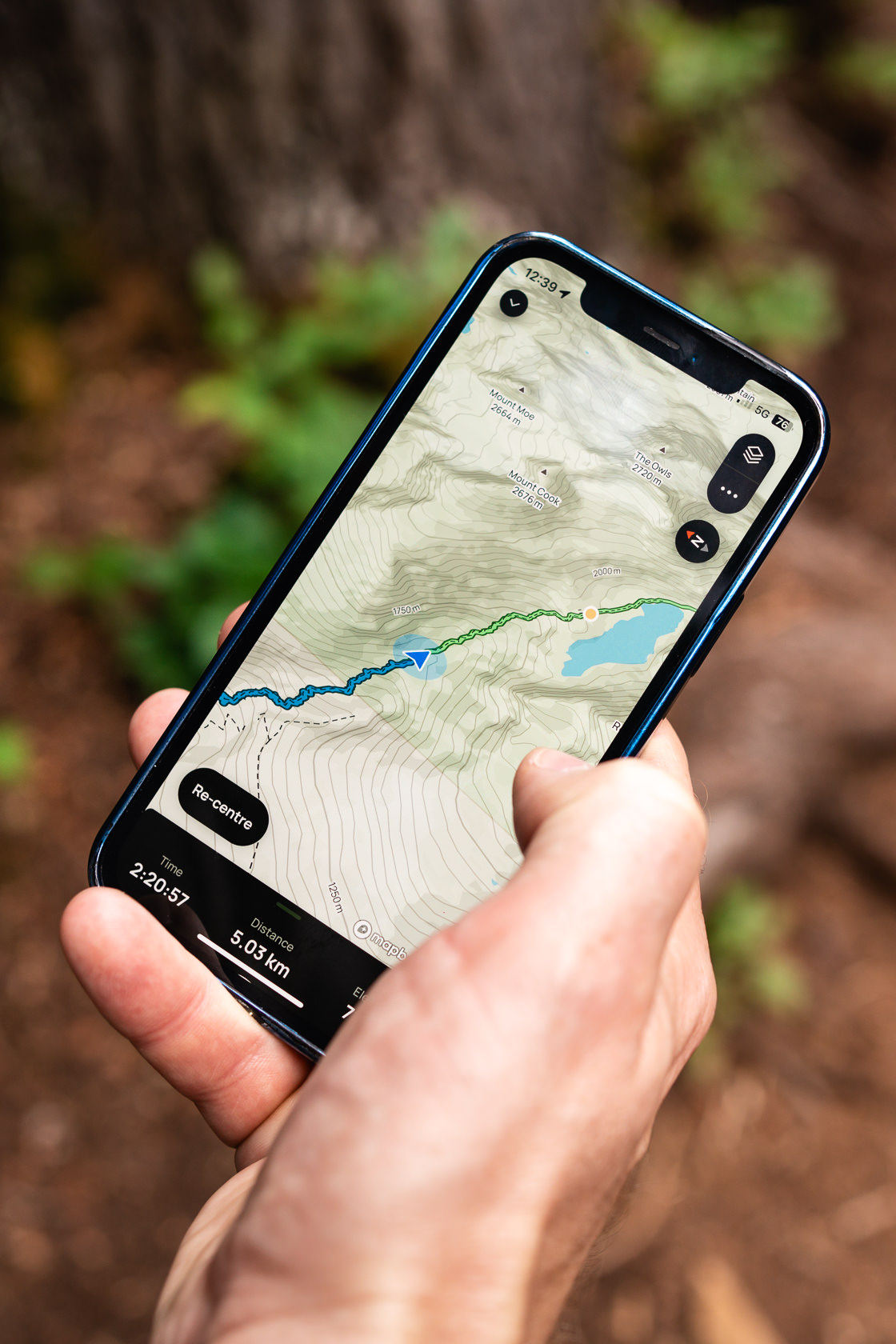 Hiker's hand holding a phone with the map of Wedgemount Lake trail while surrounded by the lush beauty of the forest