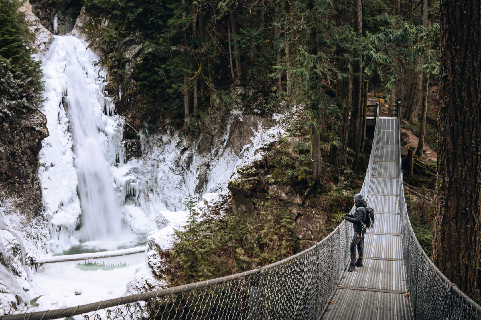 Man on a suspension bridge looking at the frozen Cascade Falls waterfall