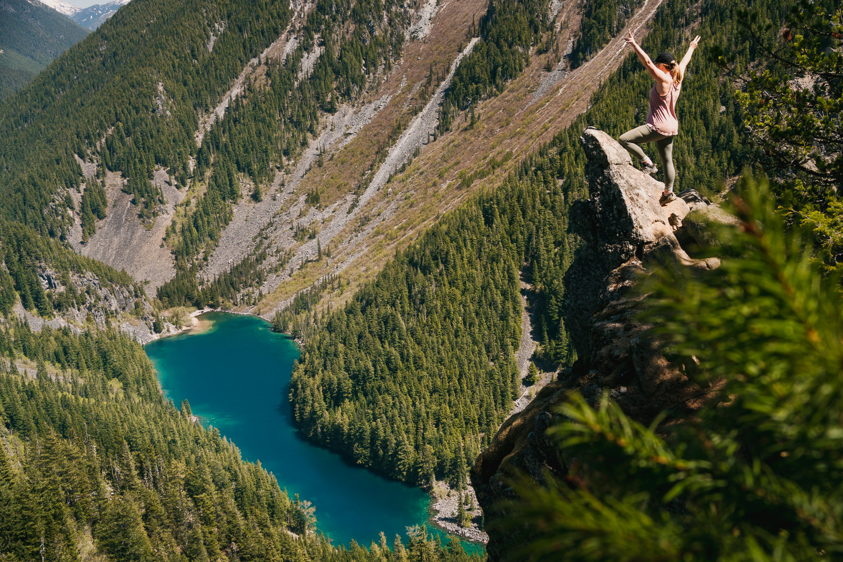 Female hiker on the Goat Ridge trail in Chilliwack, raising hands and looking at Lindeman Lake from the Porcupine Rock viewpoint