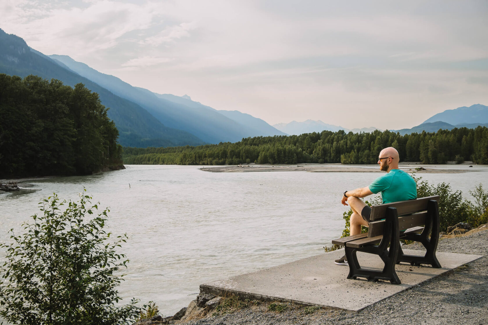 Man sitting on a bench looking towards the river and mountains in Brackendale