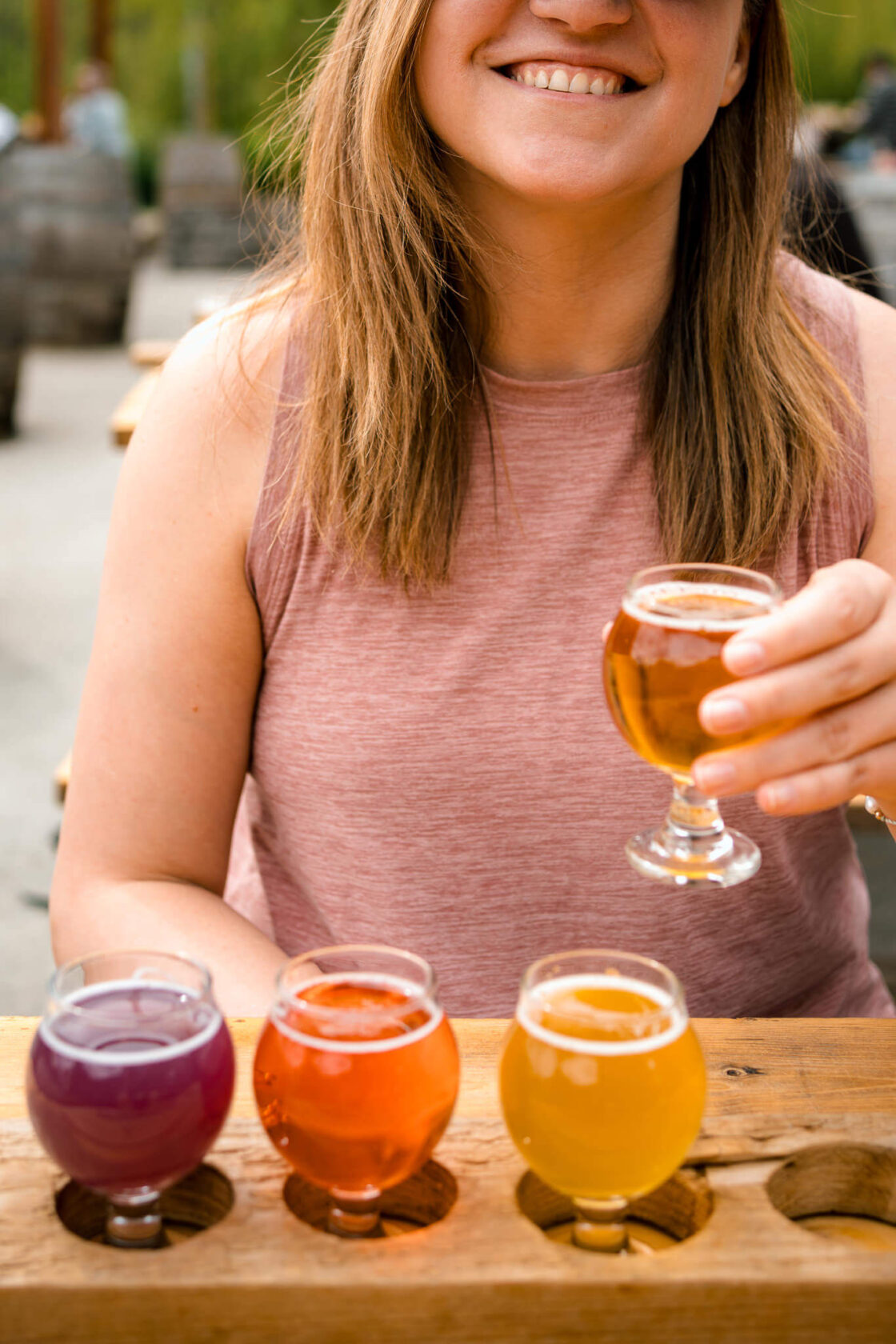 female holding a glass of beer above a flight of 4 beers 