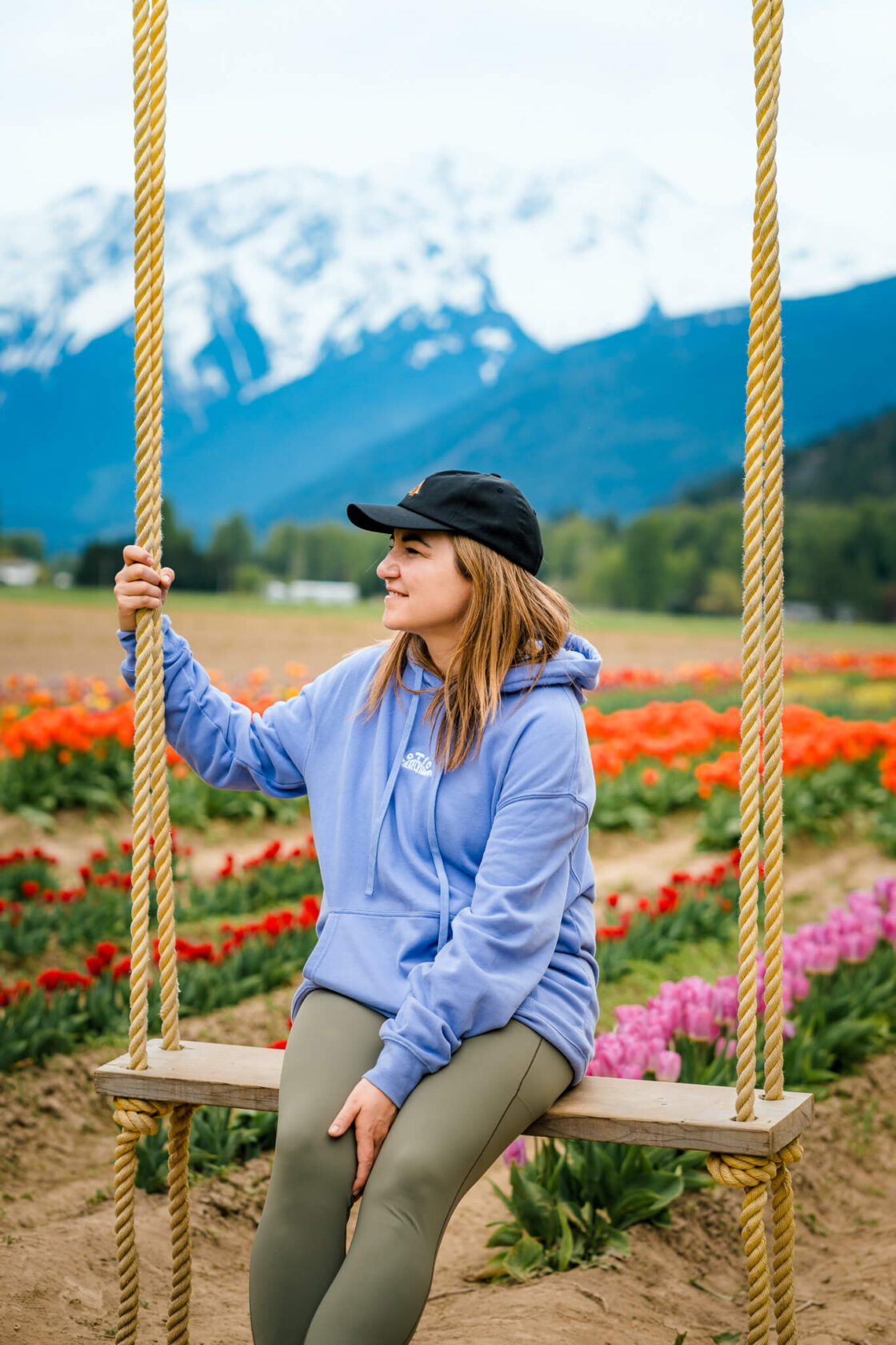 female sitting on a swing with tulip fields and mountains in the backround