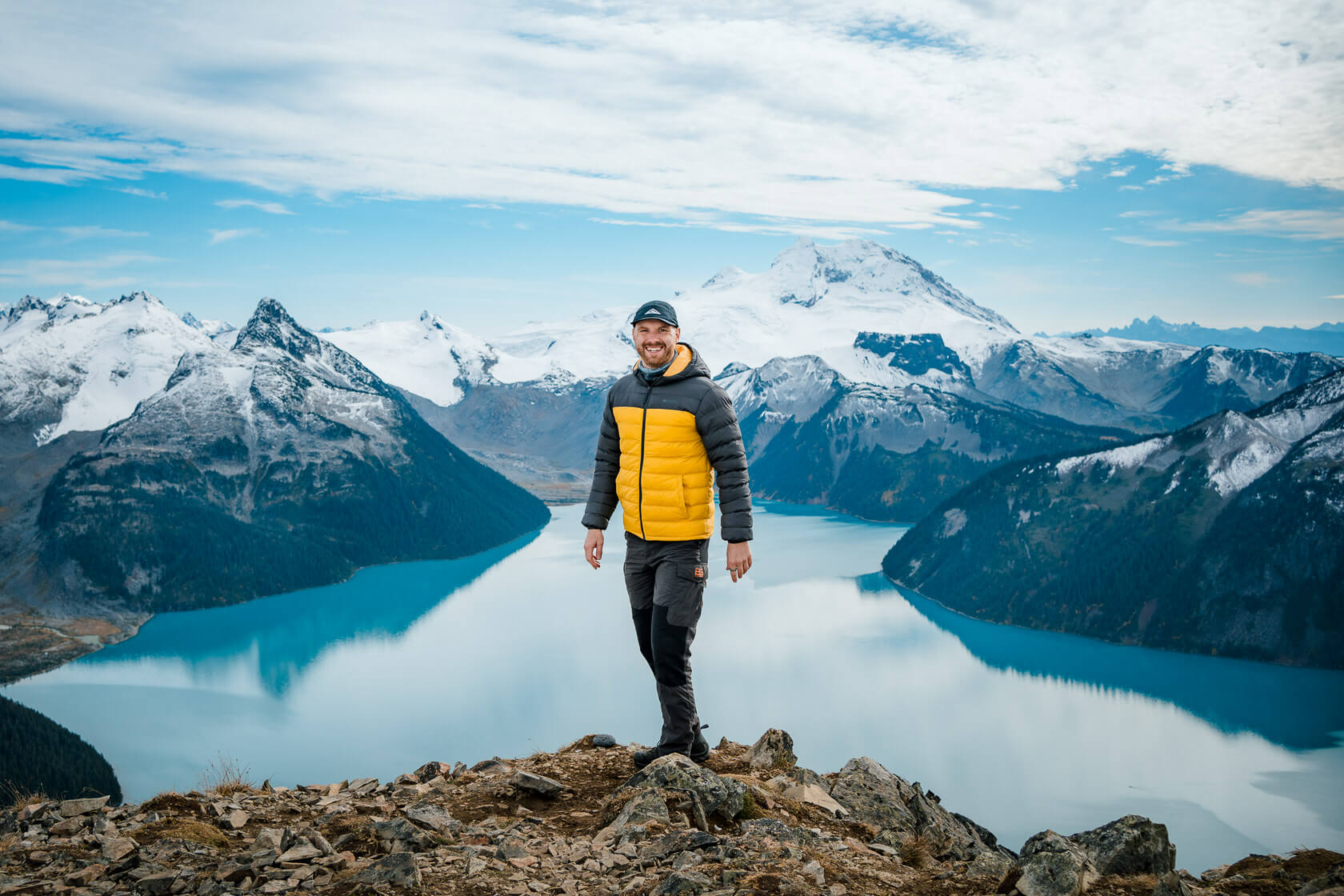 smiling hiker on top of Panorama Ridge with Garibaldi Lake in the background surrounded by snow-capped mountains