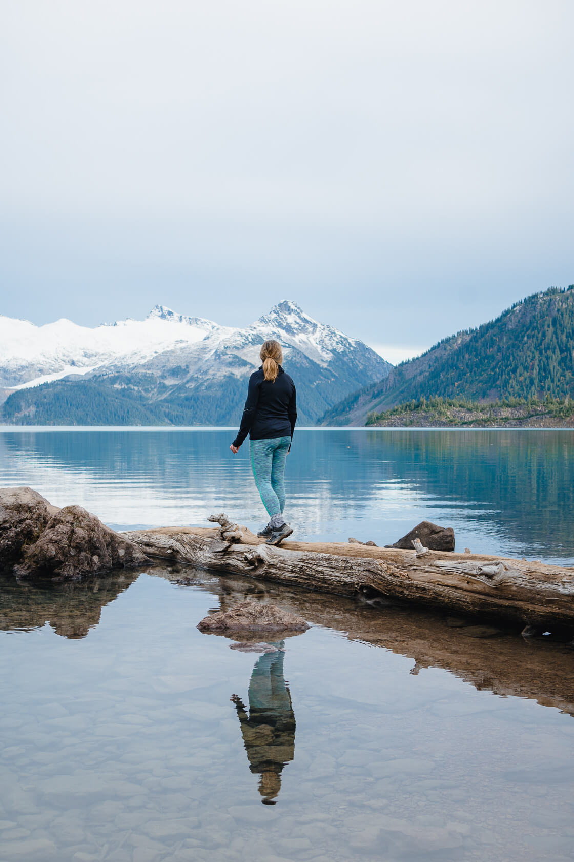 Hiker standing on a tree trunk submerged in Garibaldi Lake